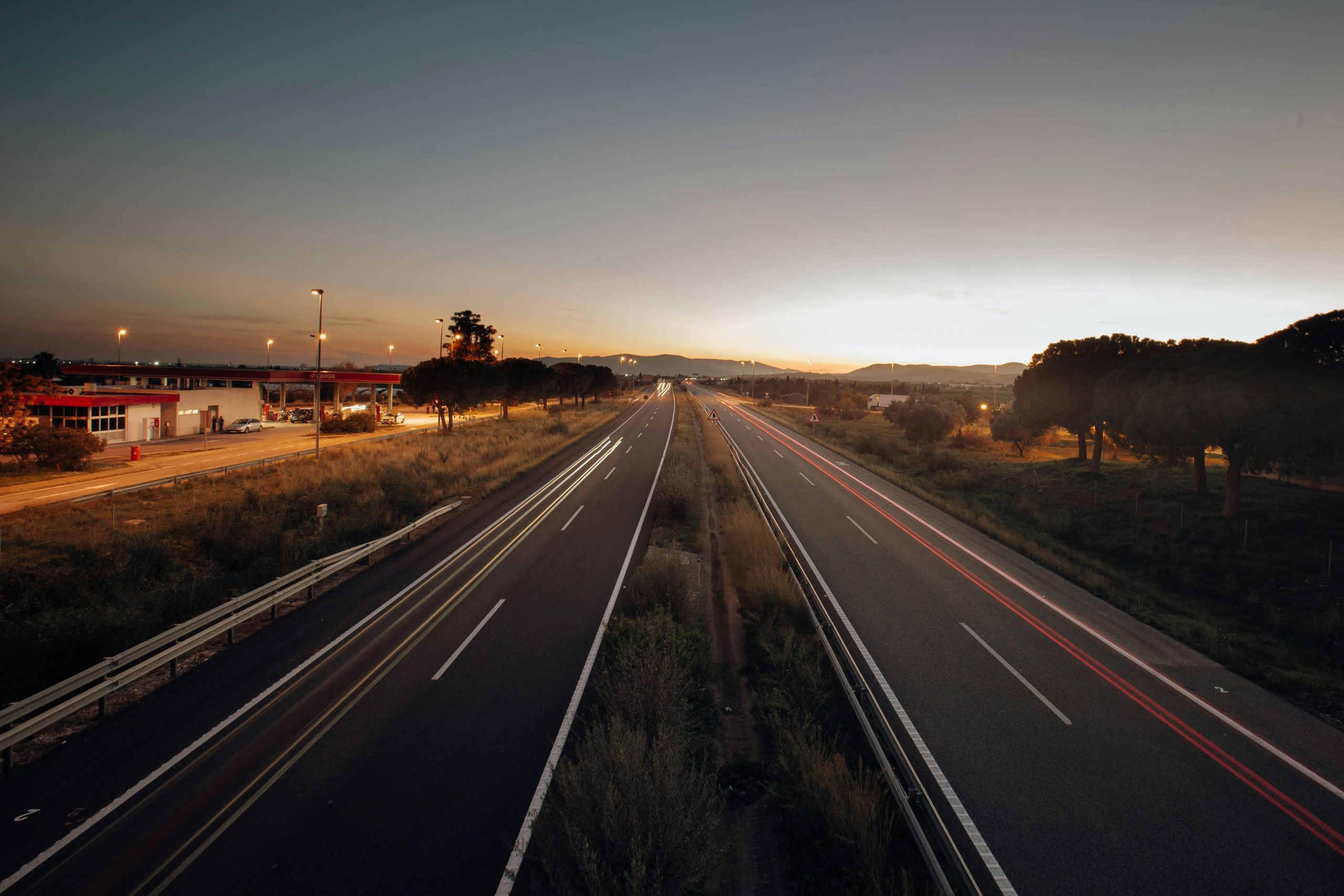 A serene expressway scene captured at sunset, with long exposure light trails and a golden horizon.